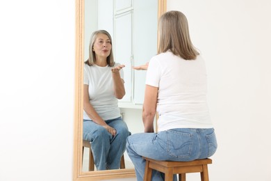 Photo of Beautiful senior woman blowing kiss near mirror indoors