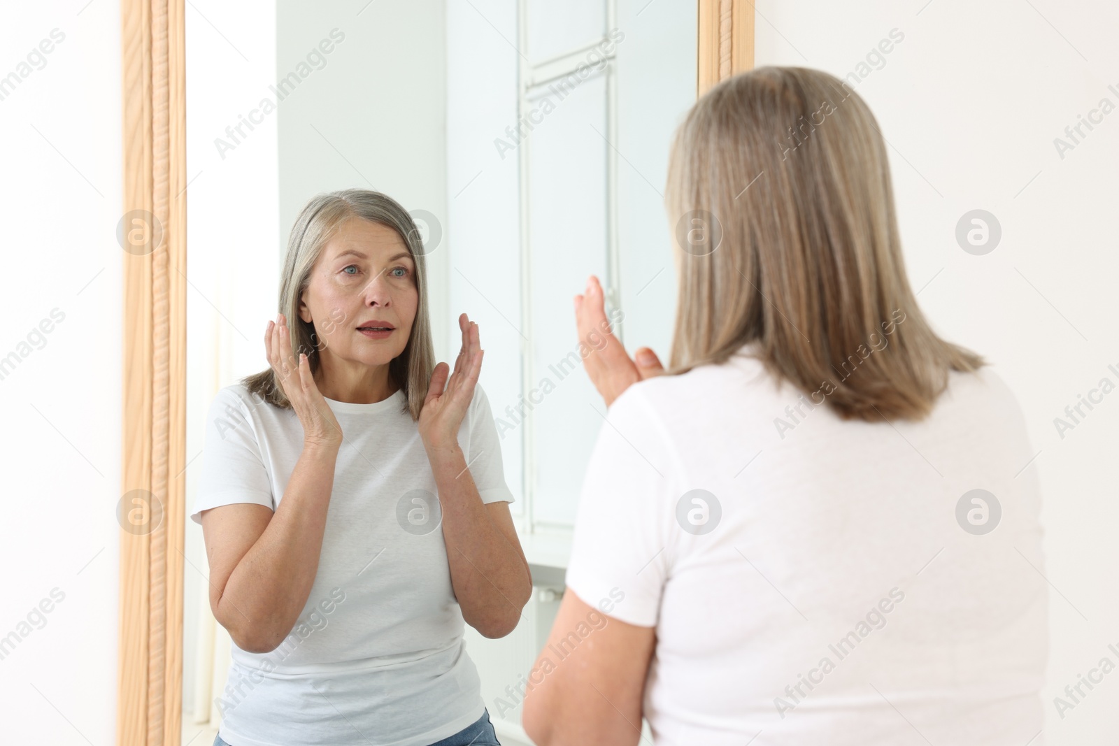 Beautiful senior woman looking at herself in mirror indoors Photo of Beautiful senior woman looking at herself in mirror indoors