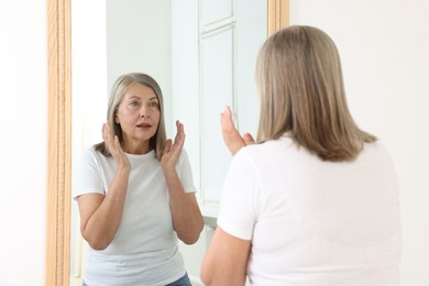 Photo of Beautiful senior woman looking at herself in mirror indoors