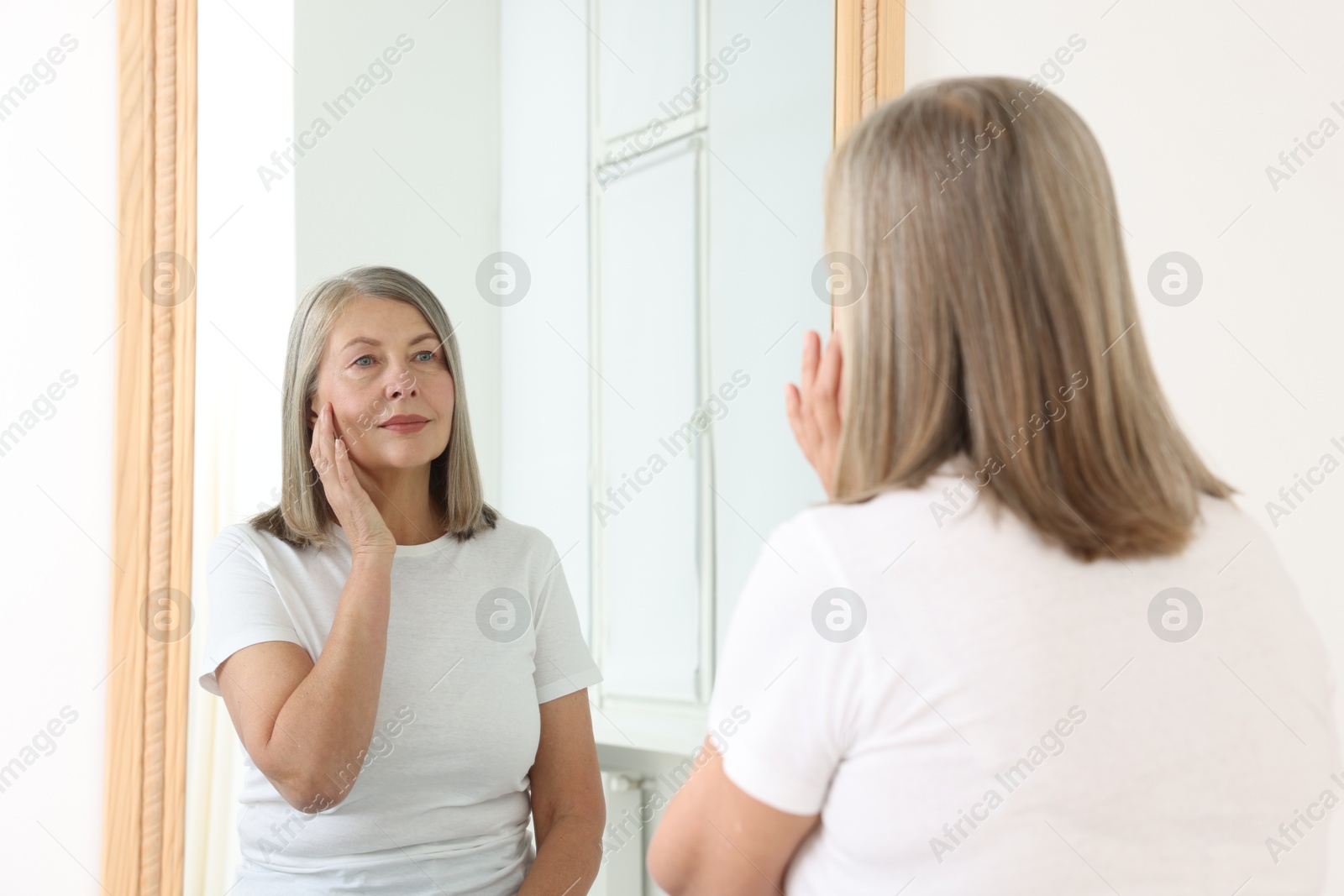 Beautiful senior woman looking at herself in mirror indoors Photo of Beautiful senior woman looking at herself in mirror indoors