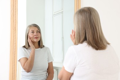 Photo of Beautiful senior woman looking at herself in mirror indoors