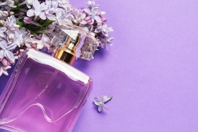 Photo of Bottle with perfume and lilac flowers on violet background, above view. Space for text
