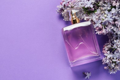Photo of Bottle with perfume and lilac flowers on violet background, flat lay. Space for text