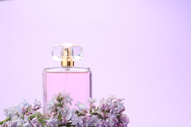 Photo of Bottle with perfume and lilac flowers on violet background, closeup. Space for text