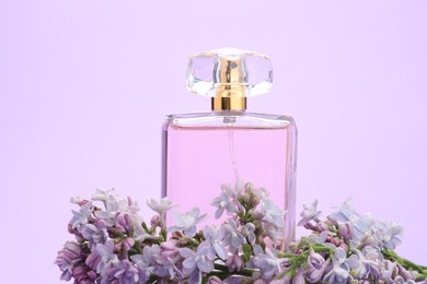 Photo of Bottle with perfume and lilac flowers on violet background, closeup