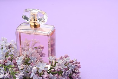 Photo of Bottle with perfume and lilac flowers on violet background, closeup. Space for text
