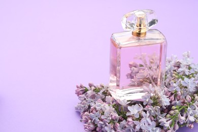 Photo of Bottle with perfume and lilac flowers on violet background, closeup. Space for text