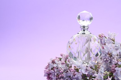 Photo of Bottle with perfume and lilac flowers on violet gradient background, closeup. Space for text