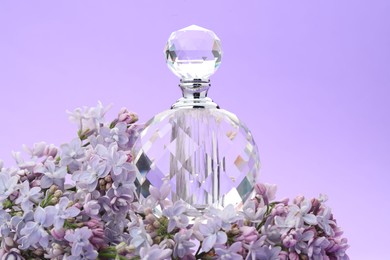 Photo of Bottle with perfume and lilac flowers on violet gradient background, closeup