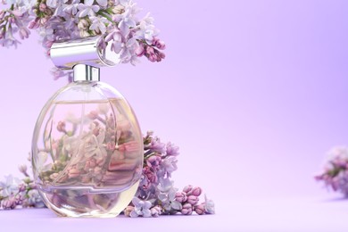 Photo of Bottle with perfume and lilac flowers on violet gradient background, closeup. Space for text