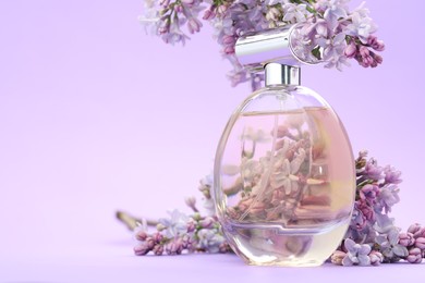 Photo of Bottle with perfume and lilac flowers on violet gradient background, closeup. Space for text