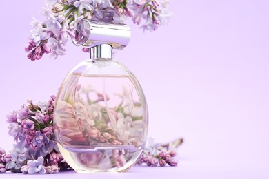 Photo of Bottle with perfume and lilac flowers on violet gradient background, closeup. Space for text
