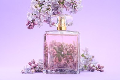 Photo of Bottle with perfume and lilac flowers on violet gradient background, closeup