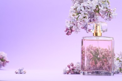 Photo of Bottle with perfume and lilac flowers on violet gradient background, closeup. Space for text