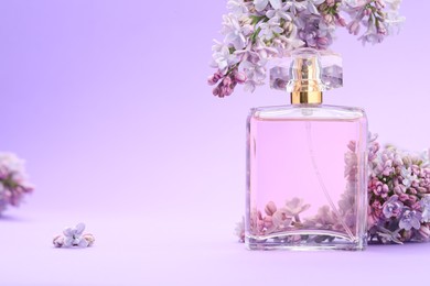 Photo of Bottle with perfume and lilac flowers on violet gradient background, closeup. Space for text