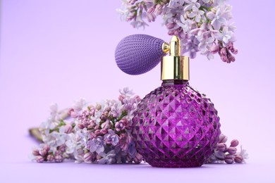 Photo of Bottle with perfume and lilac flowers on violet gradient background, closeup