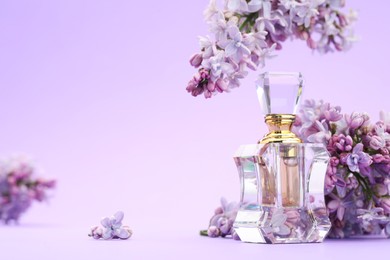 Photo of Bottle with perfume and lilac flowers on violet gradient background, closeup. Space for text