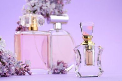 Photo of Bottles with perfumes and lilac flowers on violet background, selective focus