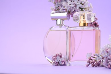 Photo of Bottles with perfumes and lilac flowers on violet background, closeup. Space for text