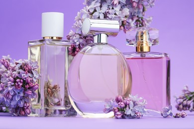 Photo of Bottles with perfumes and lilac flowers on purple gradient background, closeup