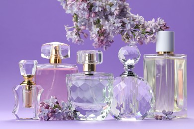 Photo of Bottles with perfumes and lilac flowers on purple gradient background, closeup
