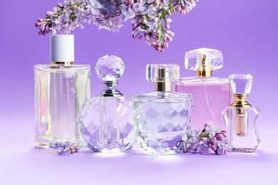 Photo of Bottles with perfumes and lilac flowers on purple gradient background, closeup