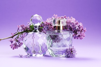 Photo of Bottles of perfumes and branch with lilac flowers on purple gradient background, closeup