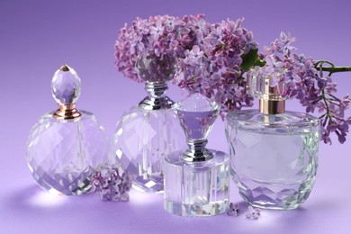 Photo of Bottles of perfumes and branch with lilac flowers on purple gradient background, closeup