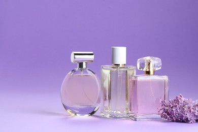 Photo of Bottles with perfumes and lilac flowers on purple gradient background, closeup. Space for text