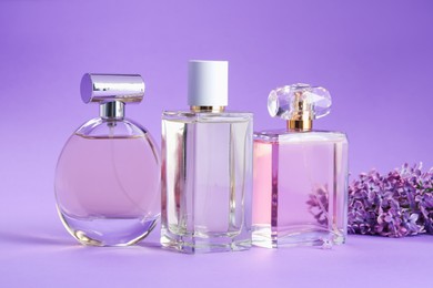 Photo of Bottles with perfumes and lilac flowers on purple gradient background, closeup