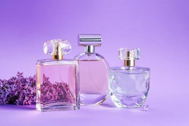 Photo of Bottles with perfumes and lilac flowers on purple gradient background, closeup