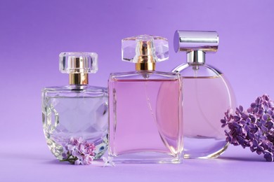 Photo of Bottles with perfumes and lilac flowers on purple gradient background, closeup