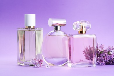 Photo of Bottles with perfumes and lilac flowers on purple gradient background, closeup