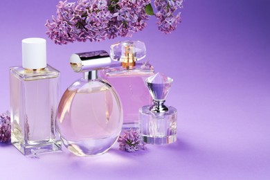Photo of Bottles with perfumes and lilac flowers on purple gradient background, closeup. Space for text