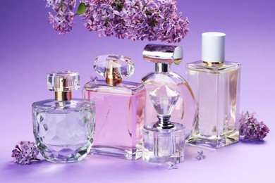 Photo of Bottles with perfumes and lilac flowers on purple gradient background, closeup
