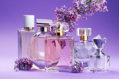 Photo of Bottles with perfumes and lilac flowers on purple gradient background, closeup