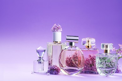 Photo of Bottles with perfumes and lilac flowers on purple gradient background, closeup. Space for text