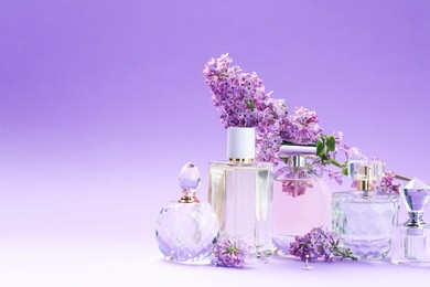 Photo of Bottles with perfumes and lilac flowers on purple gradient background, closeup. Space for text