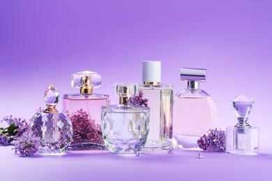 Photo of Bottles with perfumes and lilac flowers on purple gradient background, closeup