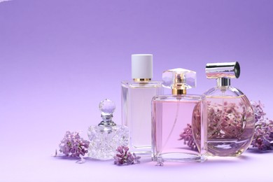 Photo of Bottles with perfumes and lilac flowers on purple gradient background, closeup. Space for text