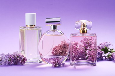 Photo of Bottles of perfumes and branches with lilac flowers on purple gradient background, closeup