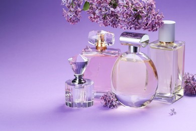 Photo of Bottles with perfumes and lilac flowers on purple gradient background, closeup. Space for text