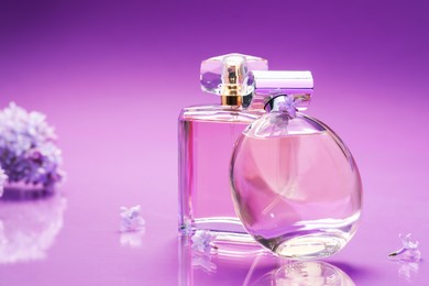 Photo of Bottles with perfumes and lilac flowers on mirror surface against color gradient background, closeup. Space for text