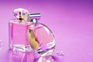 Photo of Bottles with perfumes and lilac flowers on mirror surface against color gradient background, closeup. Space for text