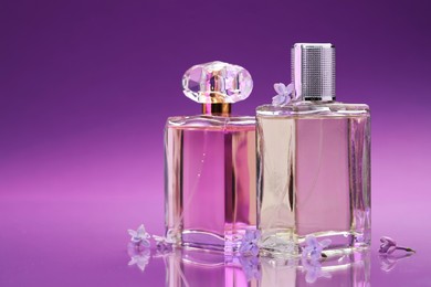 Photo of Bottles with perfumes and lilac flowers on mirror surface against color gradient background, closeup. Space for text
