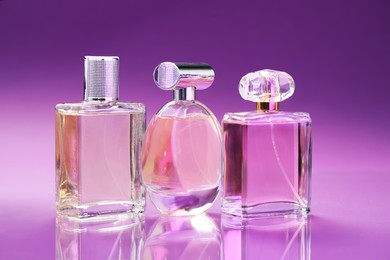 Photo of Bottles with perfumes on mirror surface against color gradient background, closeup