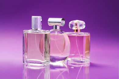 Photo of Bottles with perfumes on mirror surface against color gradient background, closeup