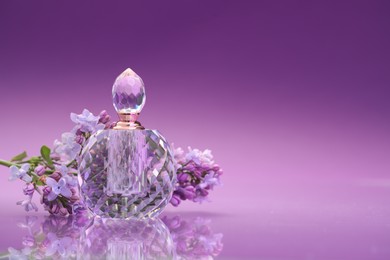 Photo of Bottle of perfume and branch with lilac flowers on mirror surface against color gradient background, closeup. Space for text