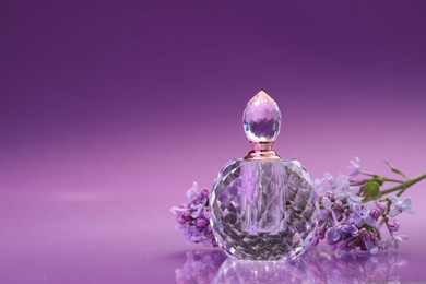 Photo of Bottle of perfume and branch with lilac flowers on mirror surface against color gradient background, closeup. Space for text