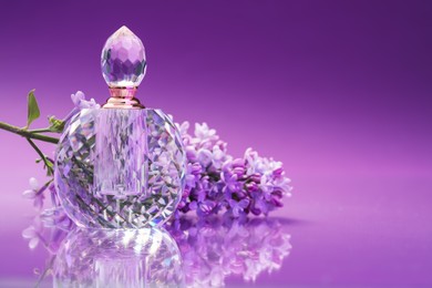 Photo of Bottle of perfume and branch with lilac flowers on mirror surface against color gradient background, closeup. Space for text